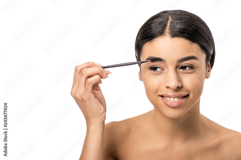 beautiful smiling african american girl combing eyebrow with brush and looking away isolated on white