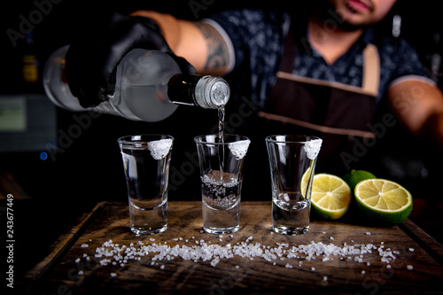 Barman pouring hard spirit into small glasses such as alcoholic shots of tequila or strong drink