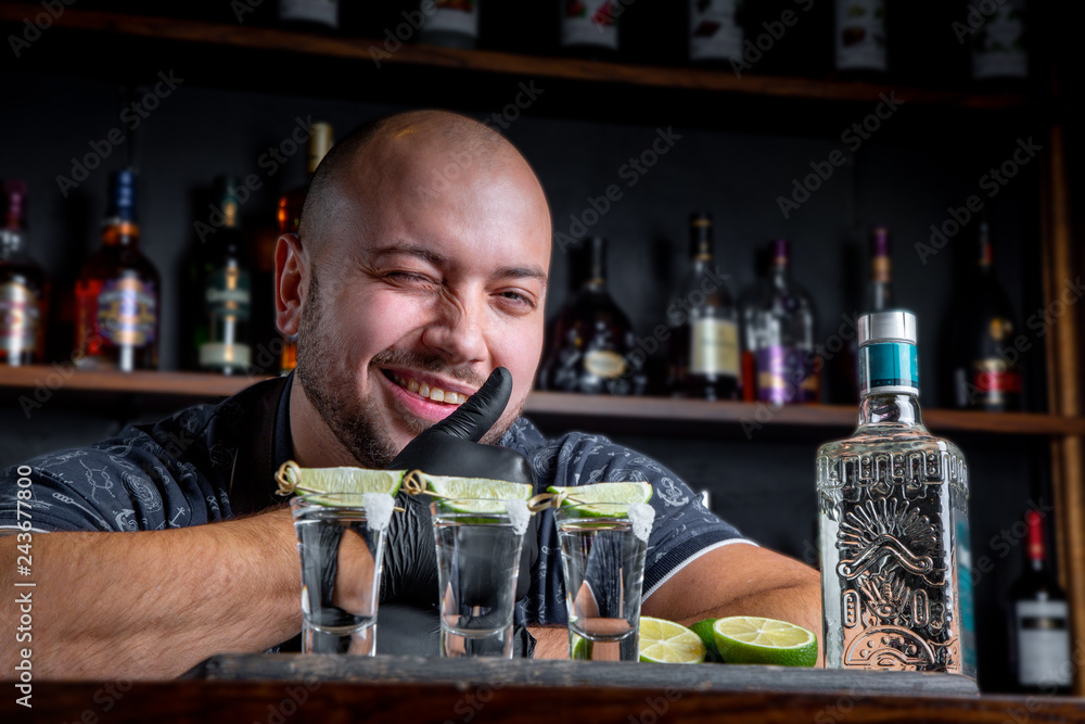 Barman pouring hard spirit into small glasses such as alcoholic shots of tequila or strong drink