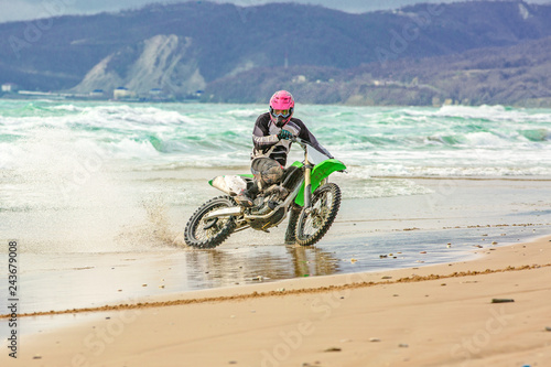 Motorcyclist in a protective suit rides a motorcycle on the sea, splashes fly from under the wheels.
