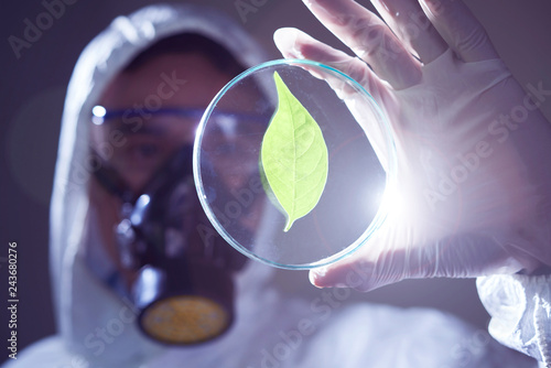 Man in biohazard costume holding petri dish with green leaf inside