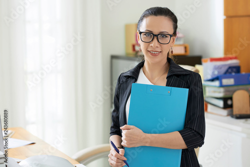Portrait of pretty Asian businesswoman with folder smiling at camera