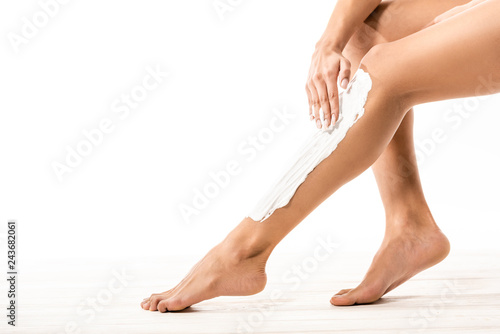 cropped shot of young african american woman applying shaving cream on leg on white