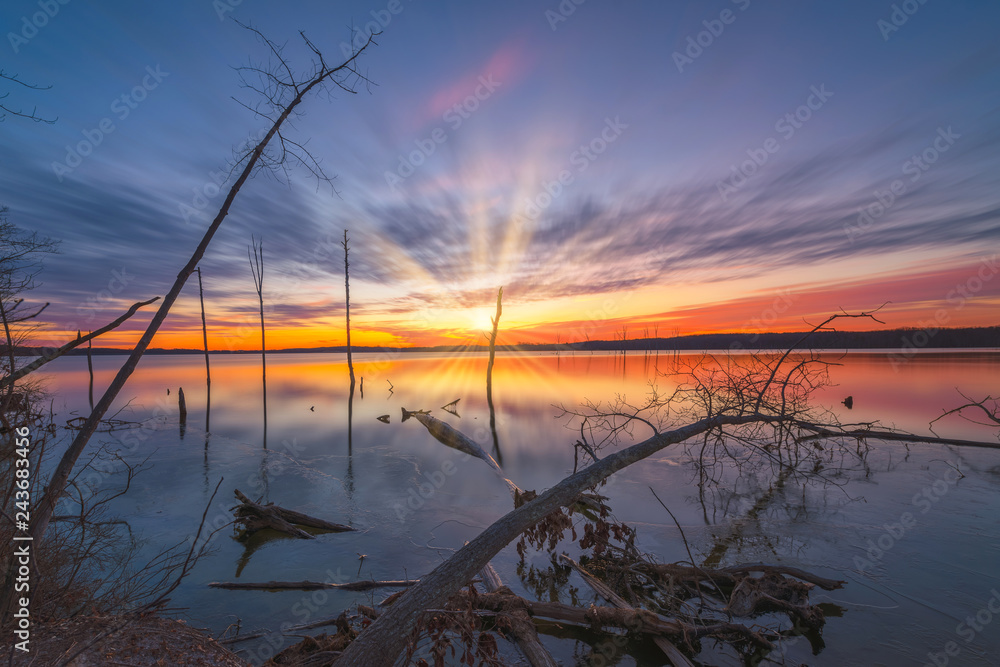 Long exposure sunrise over an icy lake with fallen trees in the foreground Long exposure sunrise over an icy lake with fallen trees in the foreground
