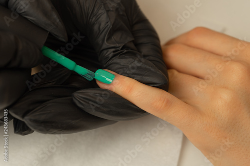 A manicurist makes manicure and covers nails with green varnish in the salon