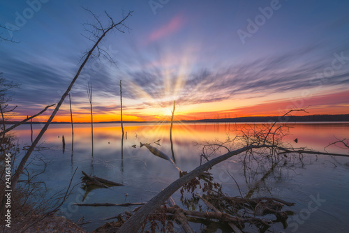 Long exposure sunrise over an icy lake with fallen trees in the foreground 