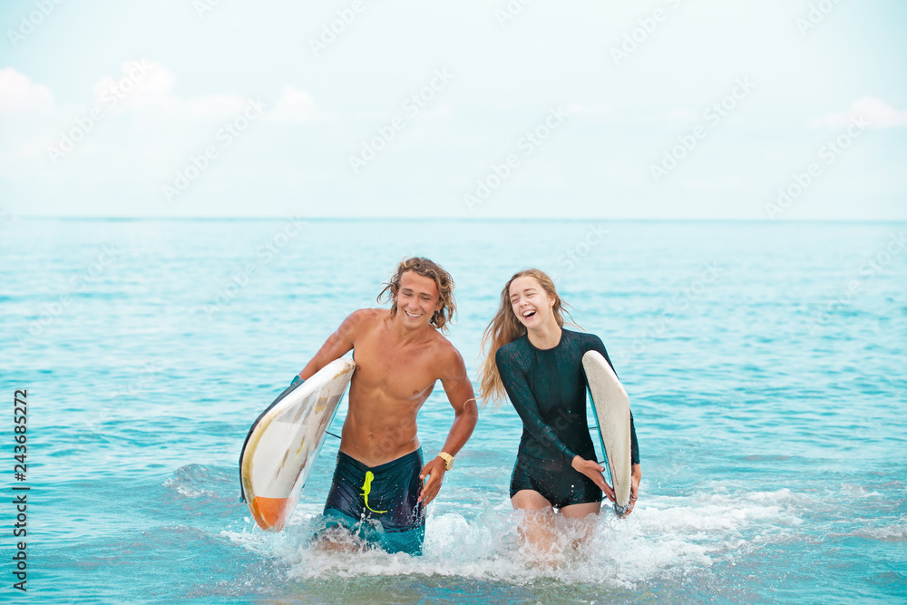 Surfers at the beach- Smiling couple of surfers walking on the beach and having fun in summer. Extreme sport and vacation concept