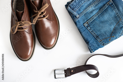 Men's outfit with brown leather shoes, jeans, and belt on white background. top view