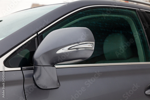Close-up of the side mirror of the car body with chrome elements in the design of a gray sedan color wet asphalt on the street, parked in the winter.