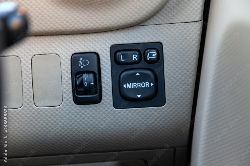 The buttons for controlling the mirrors electric drive on a stylish panel covered with perforated fair skin inside the car are of modern design in black with white signs and symbols.