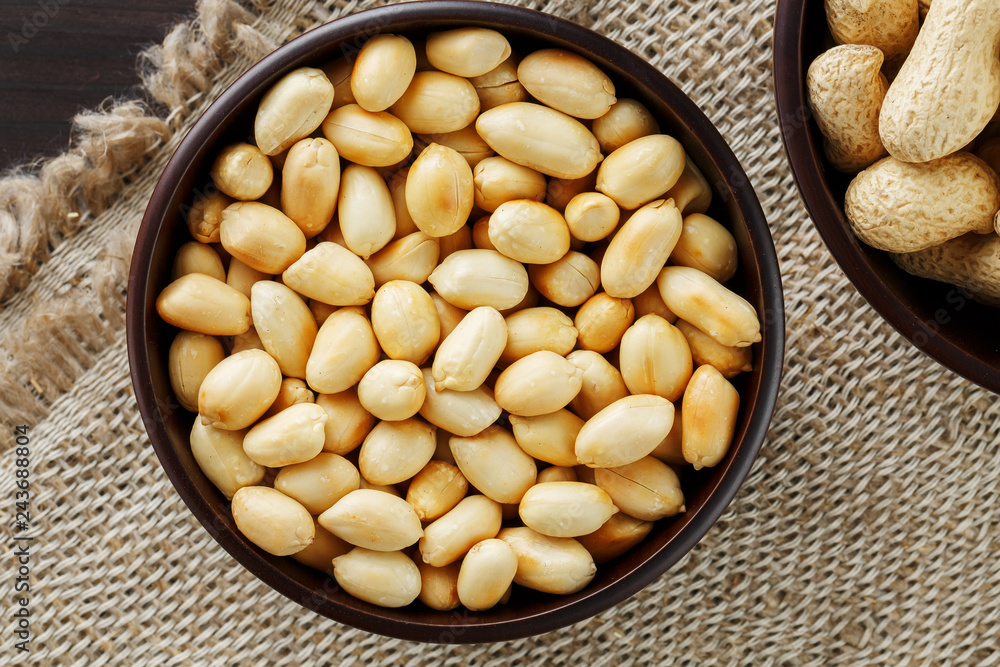 Peanuts in the shell and peeled close-up in cups. Roasted peanuts in their shells and peeled against a brown cloth. Peanuts in the shell and peeled close-up in cups. Roasted peanuts in their shells and peeled against a brown cloth.