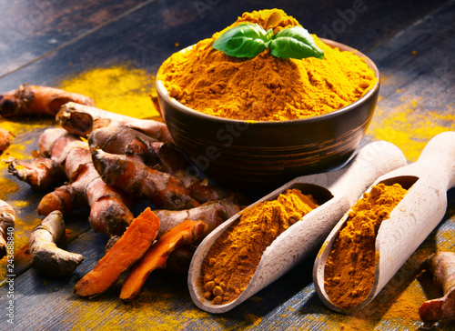 Composition with bowl of turmeric powder on wooden table