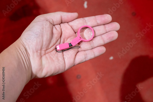 Hand holding the small pink plastic magnifier on white