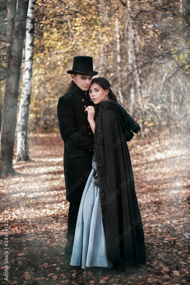 A man in a nineteenth century suit and a woman in a historical dress. Young man and woman in historical costumes in a gloomy forest A man in a nineteenth century suit and a woman in a historical dress. Young man and woman in historical costumes in a gloomy forest