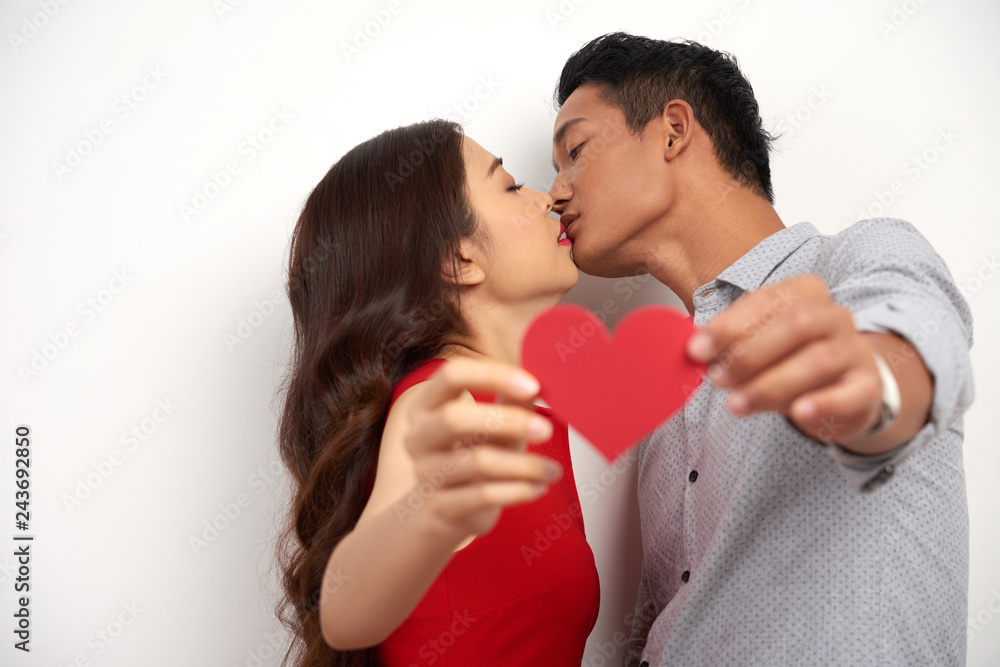 Young Asian couple in love kising and showing red paper heart