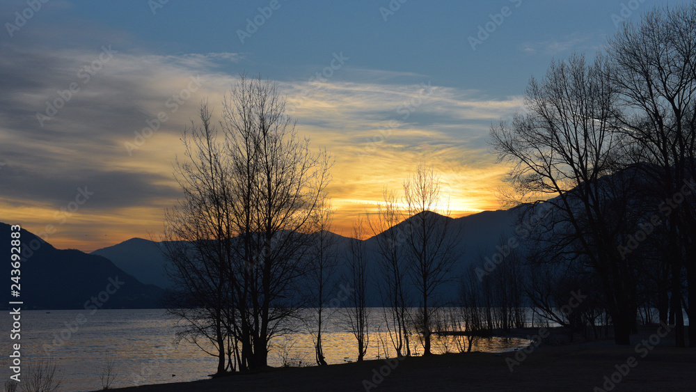 cielo al tramonto con sole dietro le montagne, sul lago e tra gli alberi