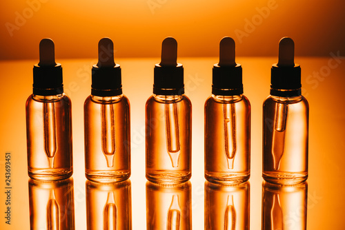 row of cbd oil in bottles with droppers on orange background photo