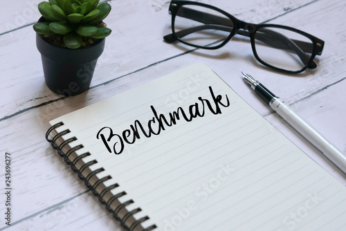 Fotografie Glasses,plant,pen and notebook written with Benchmark on white wooden background