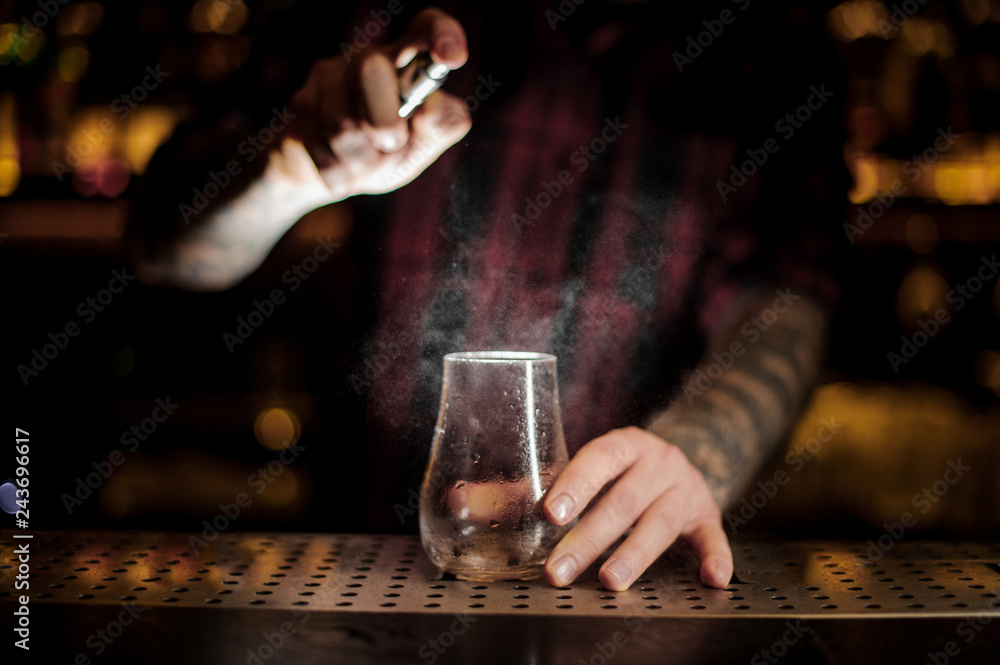 Barman sprinkling bitter into a low cocktail glass