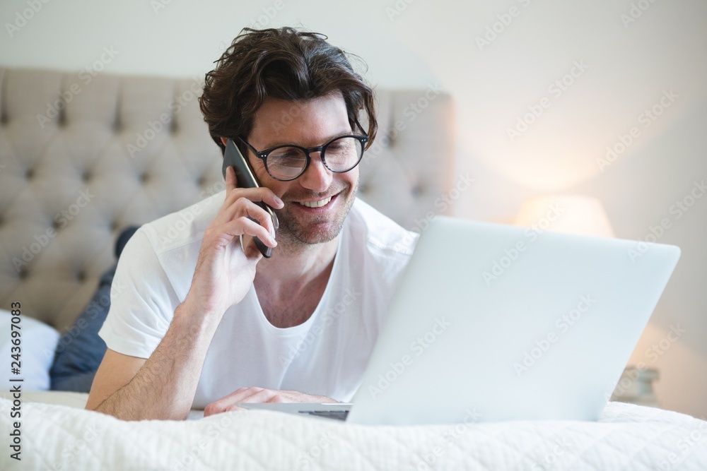 Man using laptop while talking on mobile phone