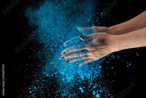 cropped view of adult woman holding blue holi powder and clapping on black background