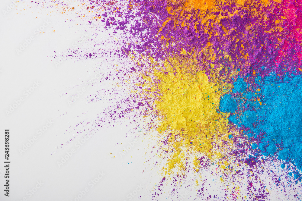 top view of explosion of yellow, purple, orange and blue holi powder on white background
