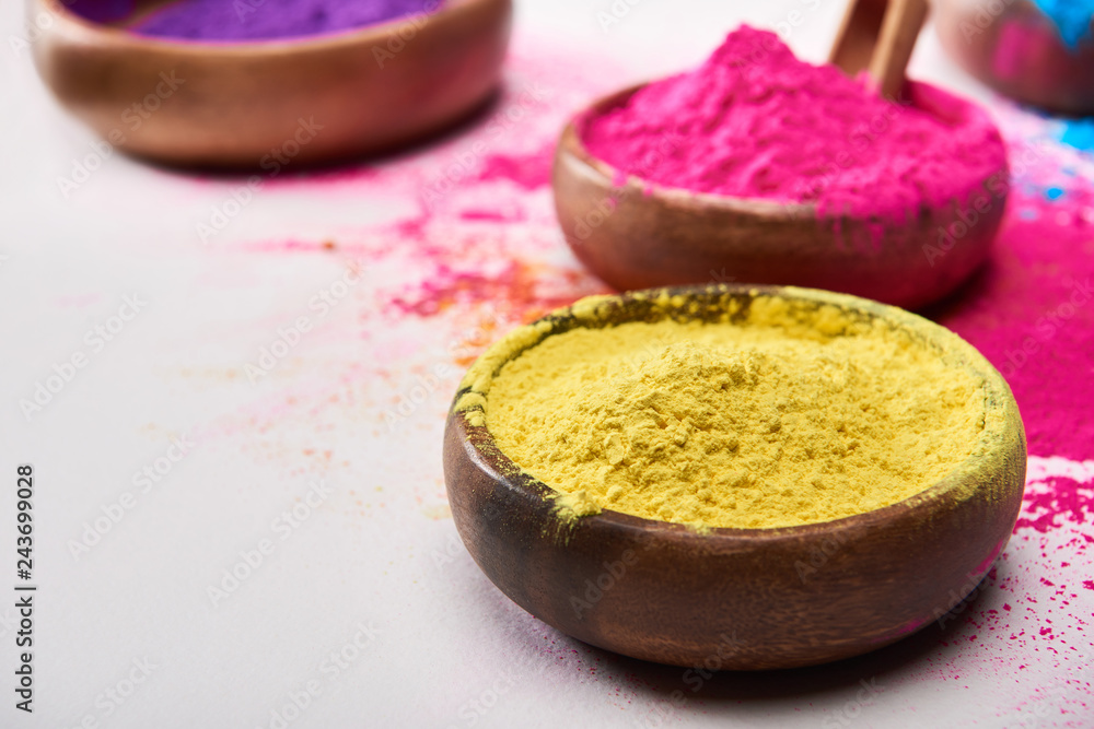 selective focus of wooden bowls with yellow, pink, blue and purple holi powder on white background selective focus of wooden bowls with yellow, pink, blue and purple holi powder on white background