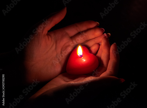 Women's hand holding a burning red candle in the dark
