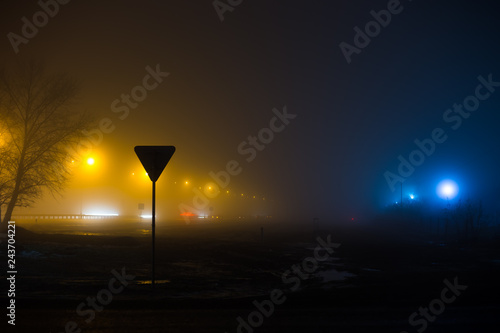 Night foggy landscape. Yellow lights along the road contrasts with cold street lighting nearby