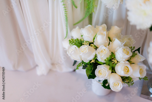 White roses in a vase with white drapery background.