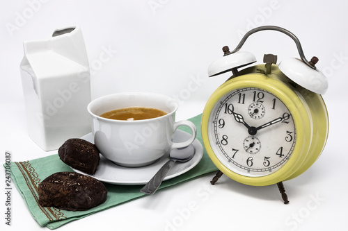 Traditional Italian breakfast with coffee and milk, cappuccino, and homemade chocolate biscuits. white ceramic cups on a white background. Vintage yellow analog alarm clock. Wake up in the morning.