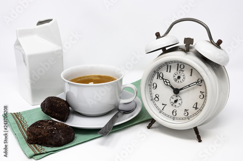 Traditional Italian breakfast with coffee and milk, cappuccino, and homemade chocolate biscuits. white ceramic cups on a white background. Vintage white analog alarm clock. Wake up in the morning.