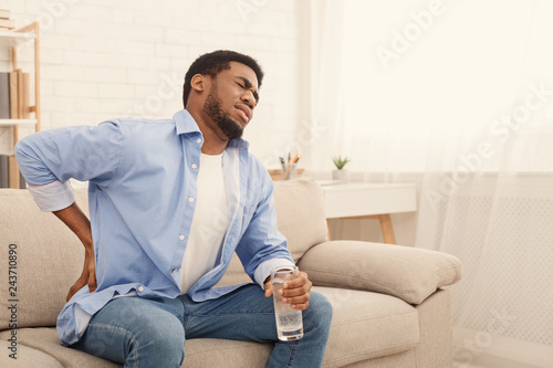 Young black man with back pain at home photo