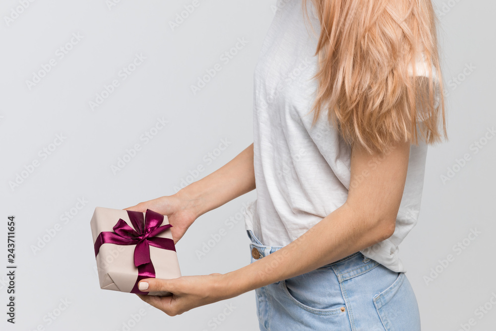 Studio portrait of cute blonde girl in white t-shirt and jeans with gift in hand/beautiful girl received a gift on Valentine's Day/pleasant surprise, gift in box, joyful glee, lovers day, wonderment. Studio portrait of cute blonde girl in white t-shirt and jeans with gift in hand/beautiful girl received a gift on Valentine's Day/pleasant surprise, gift in box, joyful glee, lovers day, wonderment.