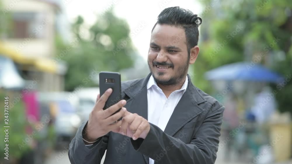 Happy bearded Indian businessman using phone outdoors Happy bearded Indian businessman using phone outdoors