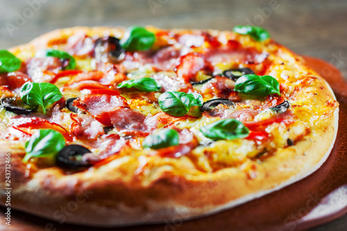 Pizza with Mozzarella cheese, ham, pepper, olive, meat, Tomato sauce, Spices and Fresh Basil. Italian pizza on wooden background