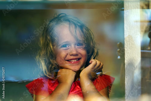 Beautiful little girl looks in the window of a shop in OIA, and makes funny faces