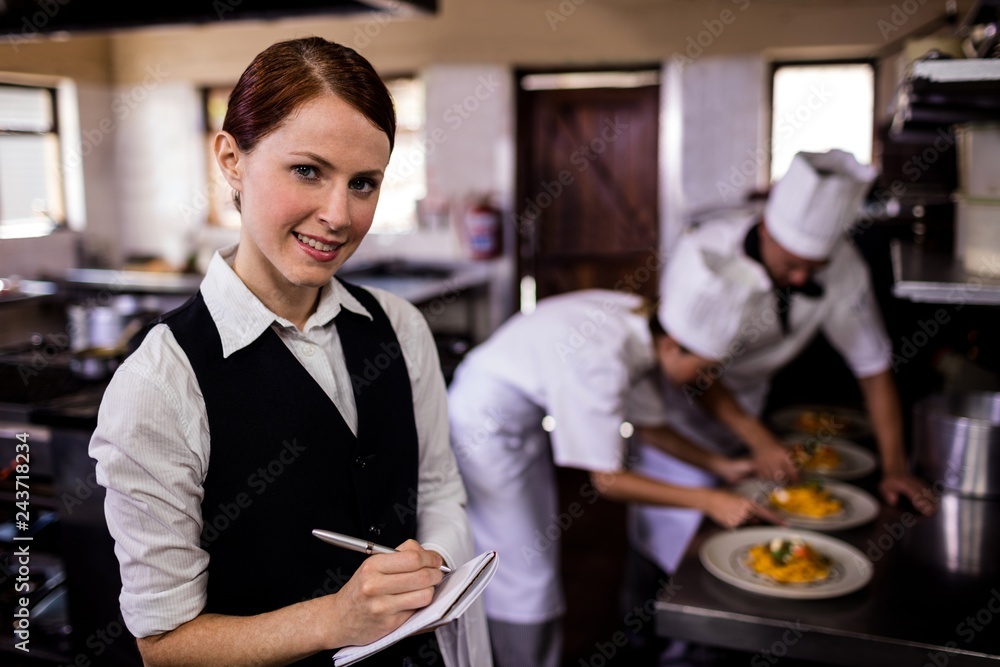 Female waitress noting an order on notepad in kitchen Female waitress noting an order on notepad in kitchen