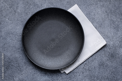 Empty black plate and white napkin on gray concrete background. Top view, with copy space