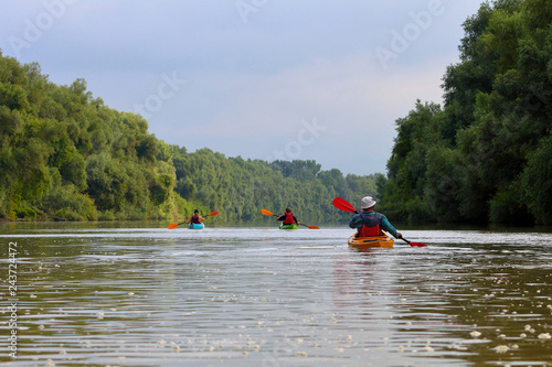 Group of friends (people) travel by kayaks. Kayaking together in wild Danube river and biosphere reserve in summer. Peacefull nature scene of calm river. Water tourism concept.