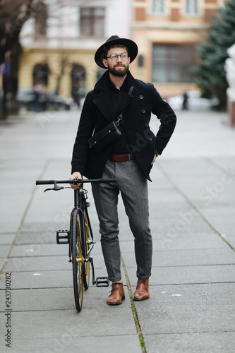 Handsome bearded young man in stylish outfit standing in the street with an fix gear bicycle