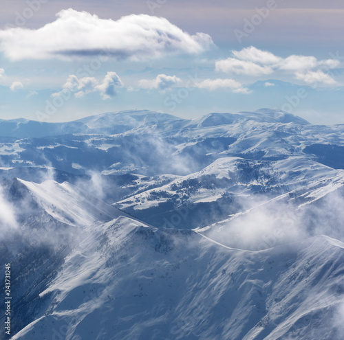 Snowy sunlight mountains in haze and cloudy sky