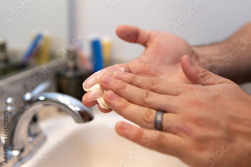 Young Caucasian Hands Squeezing Tube and Applying Acne Face Wash Lotion Skin Care Product Close Up and Zoomed In in Home Bathroom next to Sink and Mirror for Hygiene, Personal Care, and Cleanliness