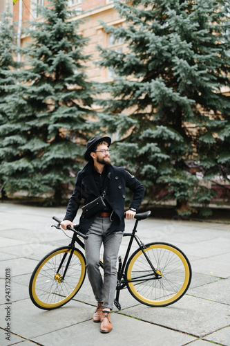 Portrait of urban hipster man in glasses and hat posing with bicycle on the street