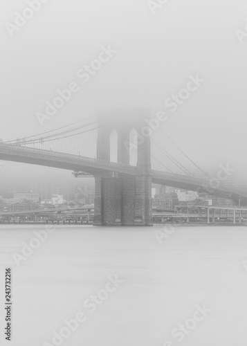 Black an white photo of Brooklyn bridge from east river on a foggy day with long exposure