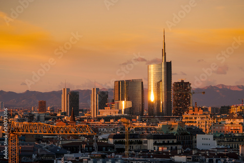 Milan skyline at sunset with modern skyscrapers in Porta Nuova business district in Italy. Panoramic view of Milano city. The mountain range of the Lombardy Alps in the background.