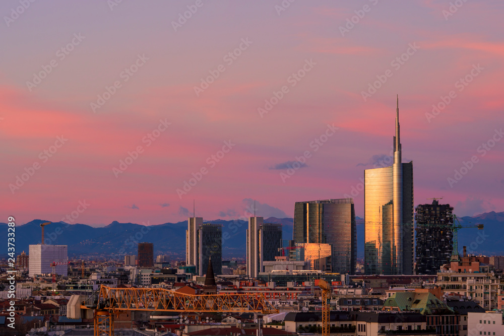 Fototapeta premium Panoramę Mediolanu o zachodzie słońca z nowoczesnymi drapaczami chmur w dzielnicy biznesowej Porta Nuova we Włoszech. Panoramiczny widok na miasto Mediolan. W tle pasmo górskie Alp Lombardii.