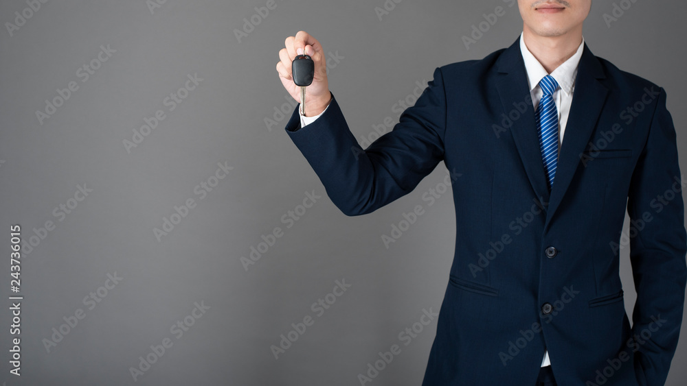 Business man is holding car key, grey background in studio Business man is holding car key, grey background in studio