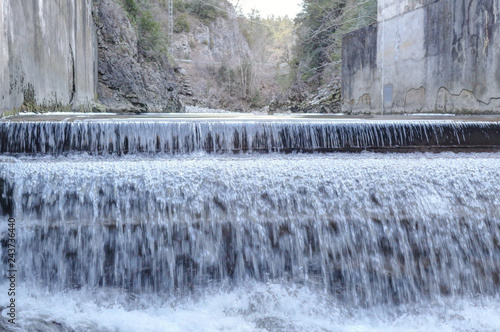 A small waterfall over concrete in the Veral river with grey rock and cold ice stalactites in the Foz de Binies zone, during winter, in Aragon, Spain