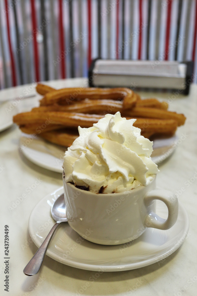 A typical spanish merienda, light meal: a cup of hot chocolate with milk cream on top of it, in front of typical Spanish fried churros A typical spanish merienda, light meal: a cup of hot chocolate with milk cream on top of it, in front of typical Spanish fried churros